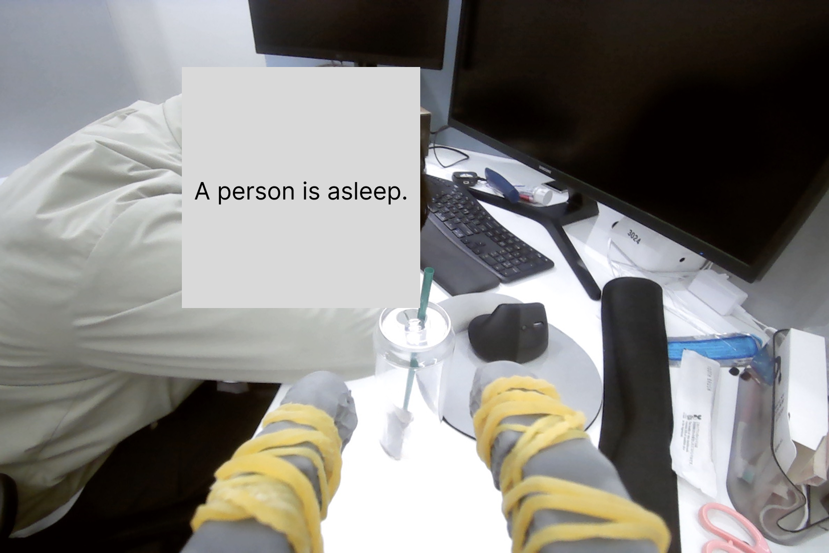First-person SO-101 arm view of a desk where a person is asleep
